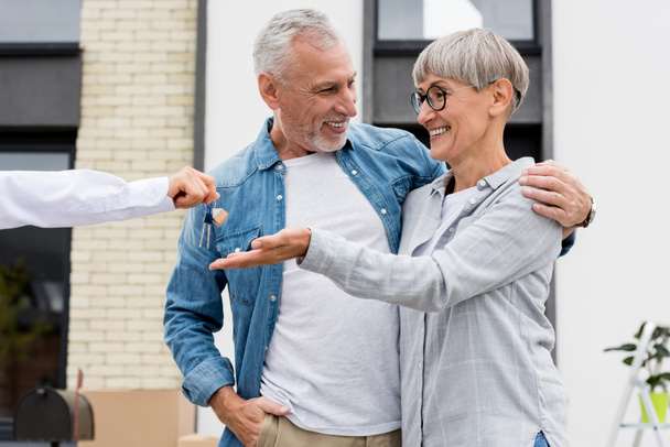 cropped view of broker giving keys of new house to smiling man and woman  - Foto, Bild