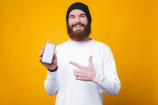 Happy young bearded man pointing at mobile screen - 写真・画像