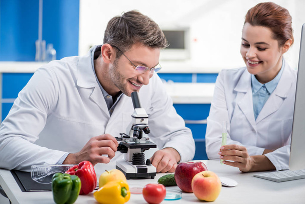 nutricionista molecular sonriente usando microscopio y su colega sosteniendo tubo de ensayo
  - Foto, Imagen