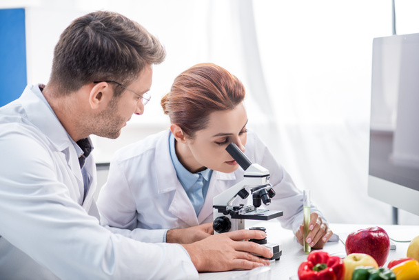 molecular nutritionist using microscope and colleague looking at her  - Photo, Image
