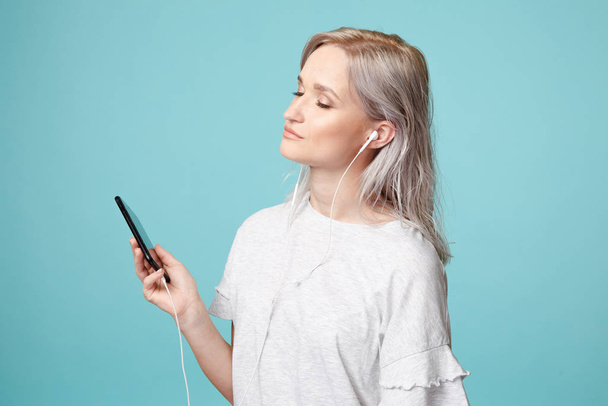 Szczęśliwa kobieta ze słuchawkami i telefonem słuchająca muzyki w studio. - Zdjęcie, obraz