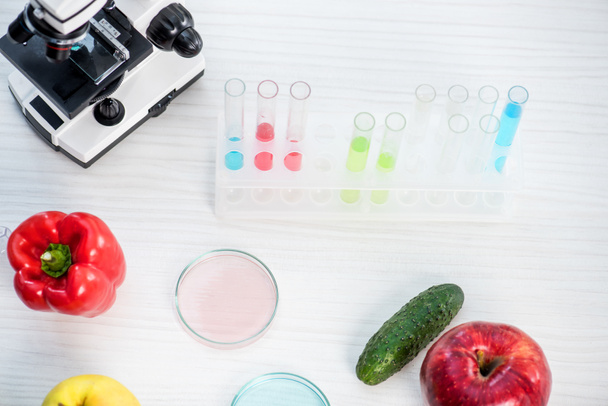 Laboratuvar masasında mikroskop, meyve, sebze, test tüpleri ve petri kaplarının yüksek açılı görüntüsü  - Fotoğraf, Görsel