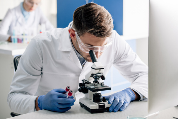 consultor genético segurando tubos de ensaio e usando microscópio em laboratório
  - Foto, Imagem