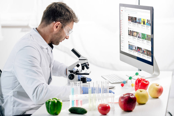 KYIV, UKRAINE - OCTOBER 4, 2019: side view of molecular nutritionist using computer with youtube website  - Foto, afbeelding