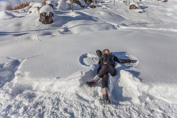 Mujer vestida de negro, feliz tumbada en la nieve
 - Foto, Imagen