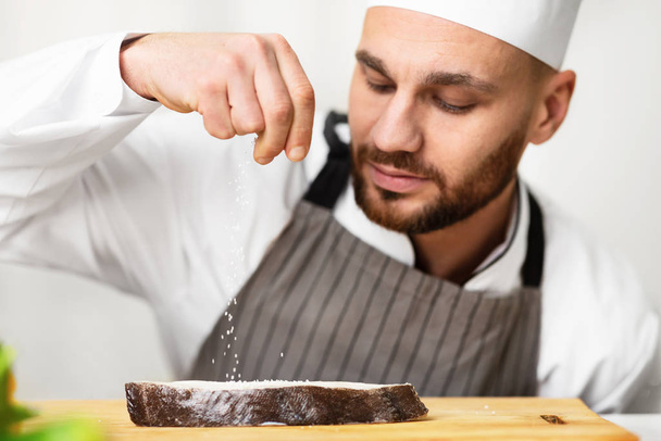 Koch Mann würzt Fisch Kochen Lebensmittel arbeiten in Restaurantküche - Foto, Bild