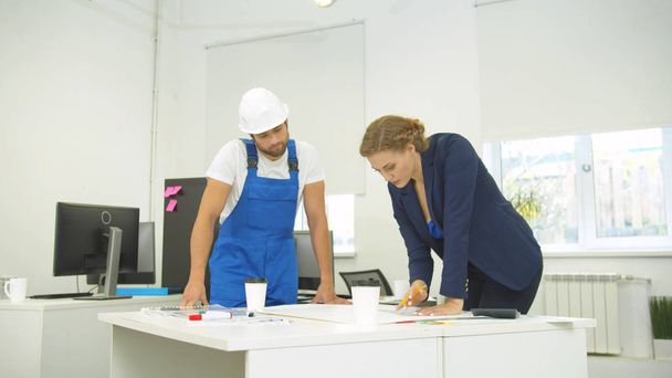 Будівельник та інженер в офісі, жінка малює на папері з олівцем та лінійкою
 - Фото, зображення