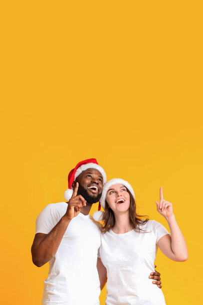 Excited interracial couple in Santa hats pointing upwards at copy space - Photo, Image