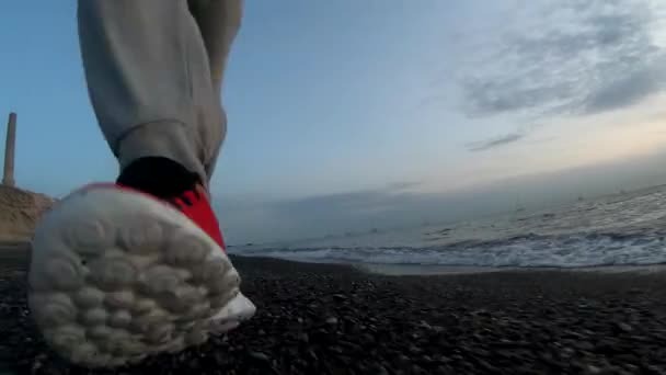 Systemem szkolenia o zachodzie słońca na plaży, sportowe nogi człowieka biegnie wzdłuż zbliżenie wody na tle kitesurferów, zwolnionym tempie. - Materiał filmowy, wideo