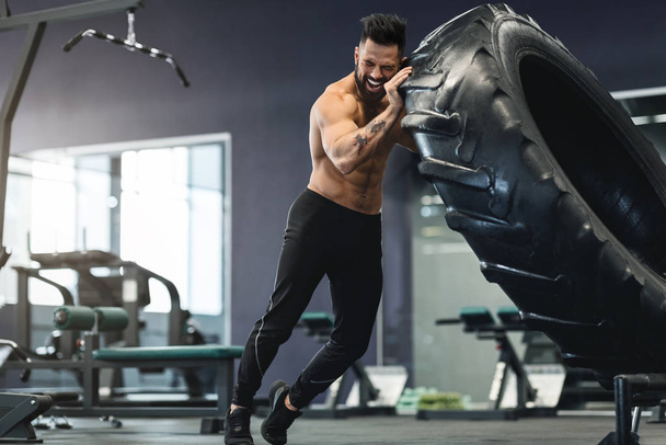 М'язистий чоловік, що працює в спортзалі, перевертає велику шину
 - Фото, зображення