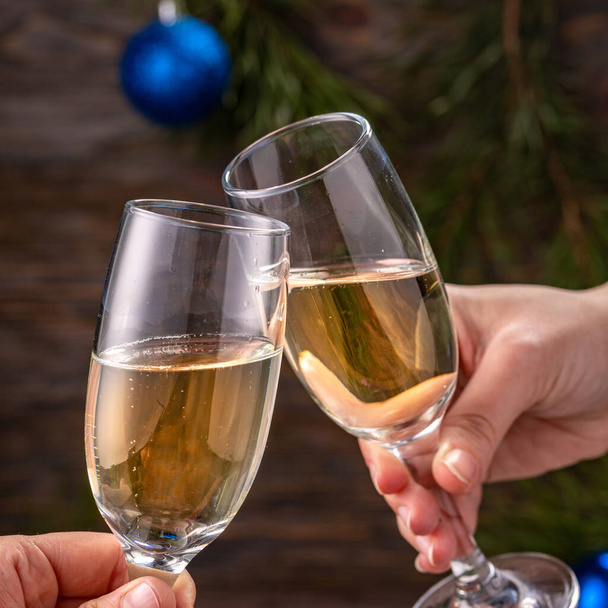 Glasses of champagne with bubbles on the background of Christmas decorations. Glasses in the hands of people touch during a festive toast. Beautiful card. Square. - Photo, Image