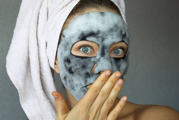  Bubble charcoal oxygen face mask. Beautiful young woman with bubbling carbonated mask and towel on the head. Face treatment. - Valokuva, kuva