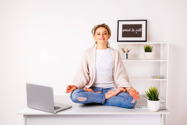 Young woman in office meditating on the table with laptop. - Фото, изображение