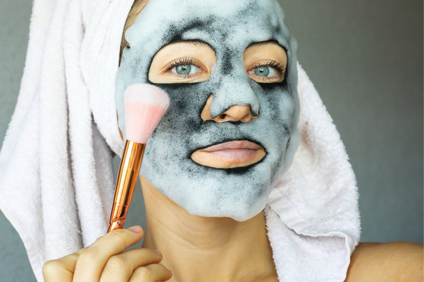  Bubble charcoal oxygen face mask. Beautiful young woman with bubbling carbonated mask and towel on the head. Face treatment. - Photo, Image