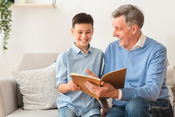 Senior Man And Boy Reading Book Sitting On Couch - Foto, afbeelding