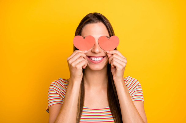 Closeup photo of funny lady holding hands little red paper hearts shy person hiding eyes flirty girlish mood wear casual striped t-shirt isolated yellow color background - Foto, Imagen