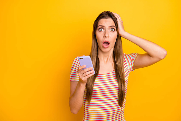 Photo of speechless pretty lady hold telephone hands reading bad news check followers arm on head wear casual striped t-shirt isolated yellow color background - Foto, immagini