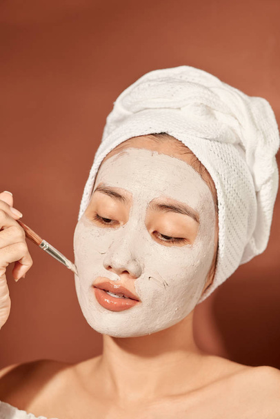 Ελκυστική γυναίκα που εφαρμόζει πήλινη μάσκα στο πρόσωπό της. - Φωτογραφία, εικόνα