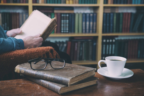 Sweet moments of relaxation with books and a cup of coffee. A man in an armchair with a cat. Vintage books, glasses, library. - Photo, image