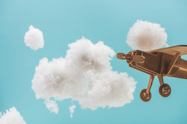 wooden toy plane flying among white fluffy clouds made of cotton wool isolated on blue - Photo, Image