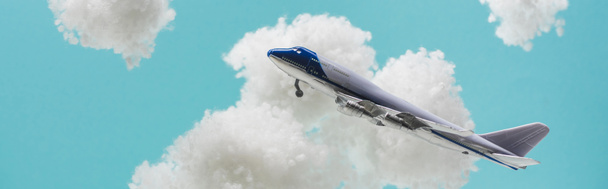 toy plane flying among white fluffy clouds made of cotton wool isolated on blue, panoramic shot - Foto, imagen