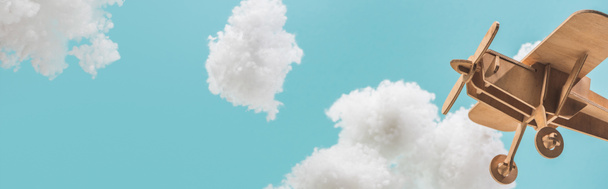 wooden toy plane flying among white fluffy clouds made of cotton wool isolated on blue, panoramic shot - Photo, image