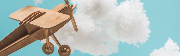 houten speelgoed vliegtuig vliegen tussen witte pluizige wolken van katoen wol geïsoleerd op blauwe, panoramische schot - Foto, afbeelding