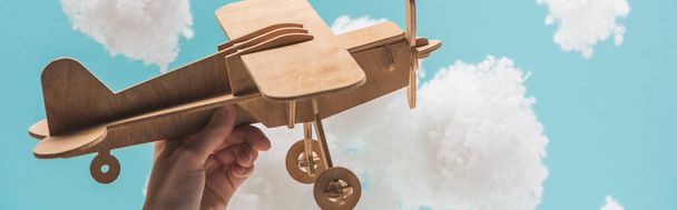 avião de brinquedo de madeira voando entre nuvens brancas fofas feitas de lã de algodão isolado em azul, tiro panorâmico
 - Foto, Imagem