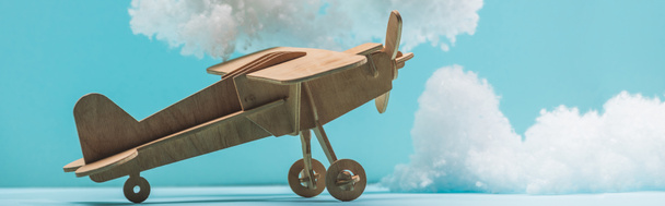 houten speelgoedvliegtuig tussen witte pluizige wolken van katoenen wol geïsoleerd op blauw, panoramisch schot - Foto, afbeelding