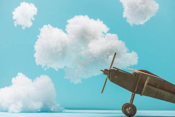 Beyaz tüylü bulutların arasında, mavi yünden yapılmış ahşap oyuncak uçak. - Fotoğraf, Görsel