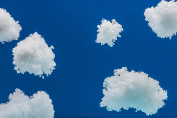 wooden toy plane flying among white fluffy clouds made of cotton wool isolated on blue - Fotografie, Obrázek