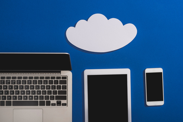 vista superior da nuvem de papel branco vazio perto de laptop, smartphone e tablet digital com tela em branco isolado em azul
 - Foto, Imagem