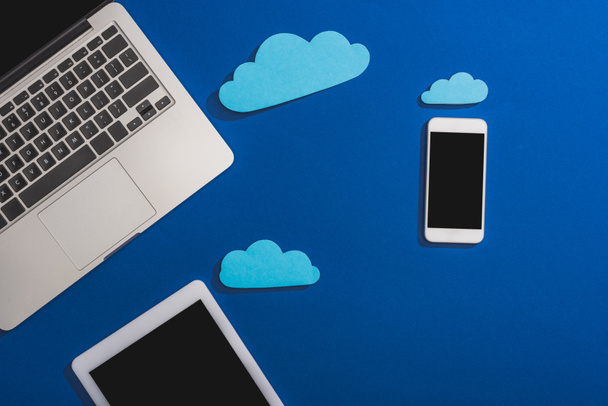 top view of empty paper clouds near laptop, smartphone and digital tablet with blank screen isolated on blue - Fotoğraf, Görsel
