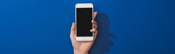 cropped view of woman holding smartphone on blue background, panoramic shot - Fotó, kép