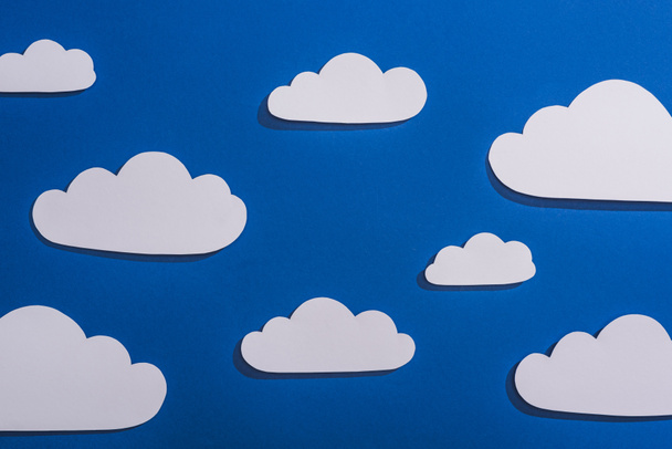 top view of white paper cut clouds on blue background - Fotoğraf, Görsel
