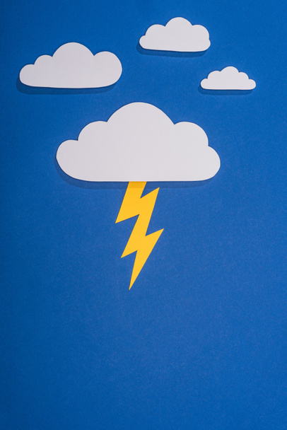 top view of white paper cut clouds with lighting on blue background - Photo, Image