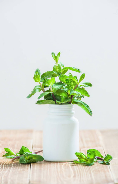 Φύλλα πράσινου φυτού σε λευκό ιατρικό μπουκάλι κοντά σε ξύλινο τραπέζι - Φωτογραφία, εικόνα