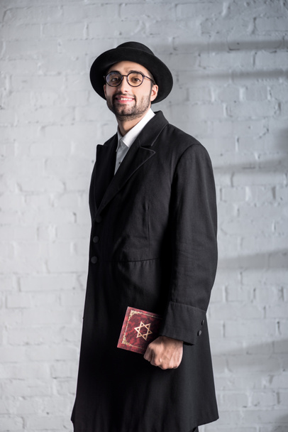 handsome and smiling jewish man in glasses holding tanakh  - Photo, image