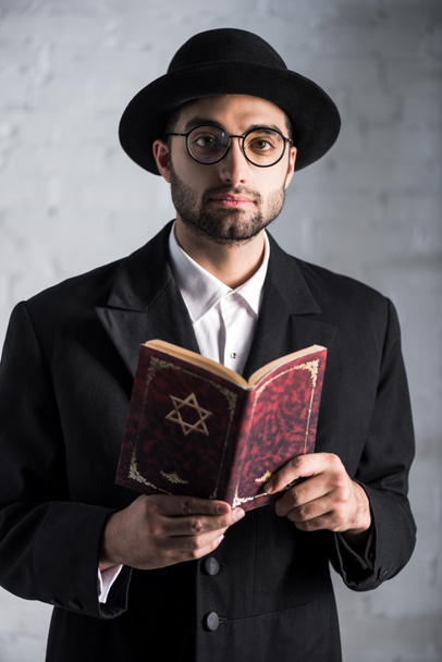 handsome and young jewish man in glasses holding tanakh  - Fotografie, Obrázek