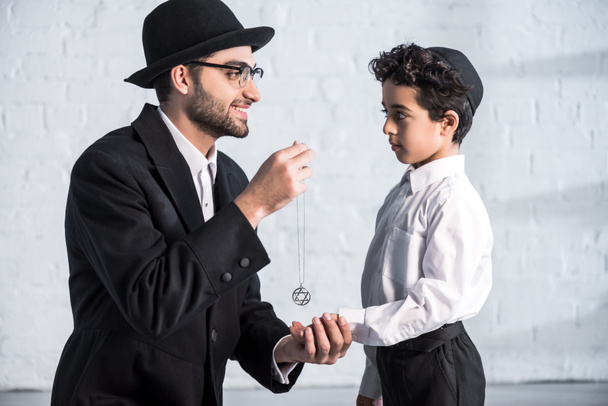 side view of smiling jewish father giving star of david necklace to son  - Foto, Bild