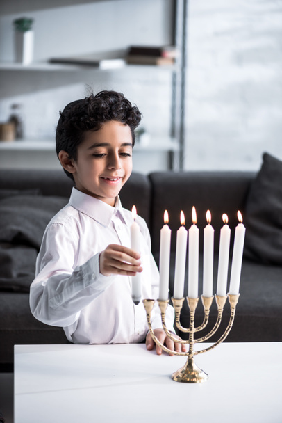 cute and smiling jewish boy in shirt holding candle  - Fotó, kép