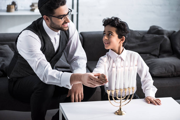 mosolygó zsidó apa és fia kezében gyertya a lakásban  - Fotó, kép