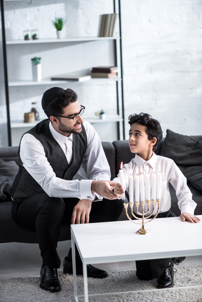 smiling jewish father and son holding candle in apartment  - Photo, Image