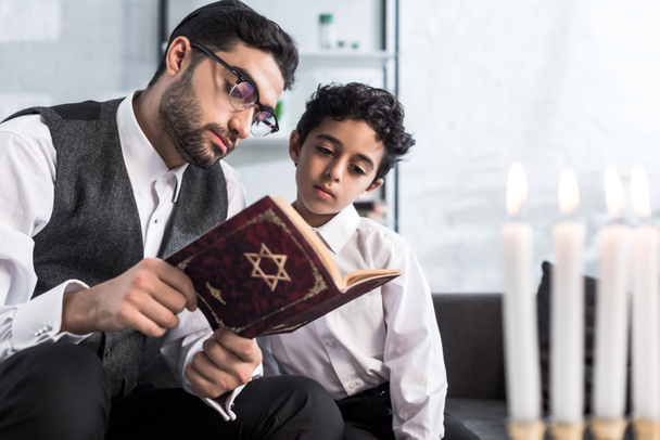όμορφος Εβραίος πατέρας και γιος διαβάζουν τανάκ στο διαμέρισμα.  - Φωτογραφία, εικόνα