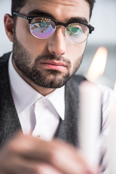 επιλεκτική εστίαση του όμορφου Εβραίου άνδρα σε γυαλιά κρατώντας κερί  - Φωτογραφία, εικόνα