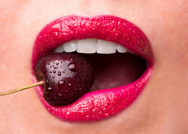 Batom vermelho em lábios e uma cereja com gotas de água. A menina
  - Foto, Imagem