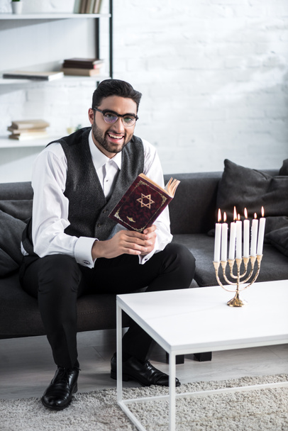 handsome and smiling jewish man in glasses holding tanakh  - Фото, изображение