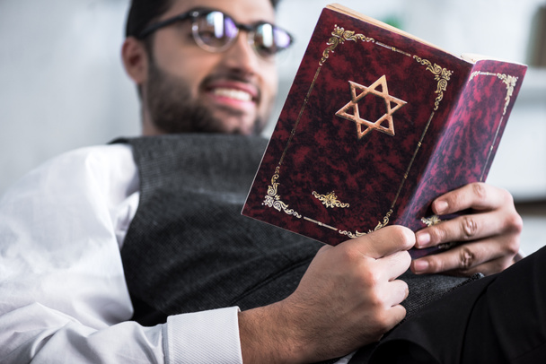 selective focus of smiling jewish man in glasses reading tanakh  - Foto, Bild