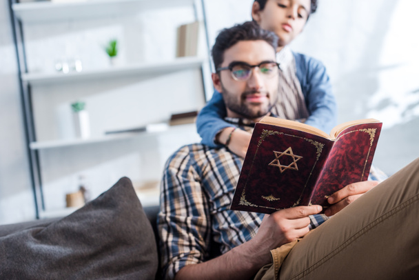 selective focus of jewish father and son reading tanakh in apartment  - Photo, Image