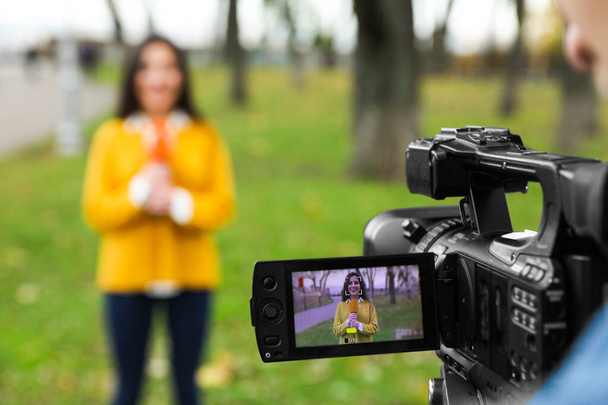 Młody dziennikarz i operator wideo pracujący w parku, skupiający się na wyświetlaczu kamery - Zdjęcie, obraz